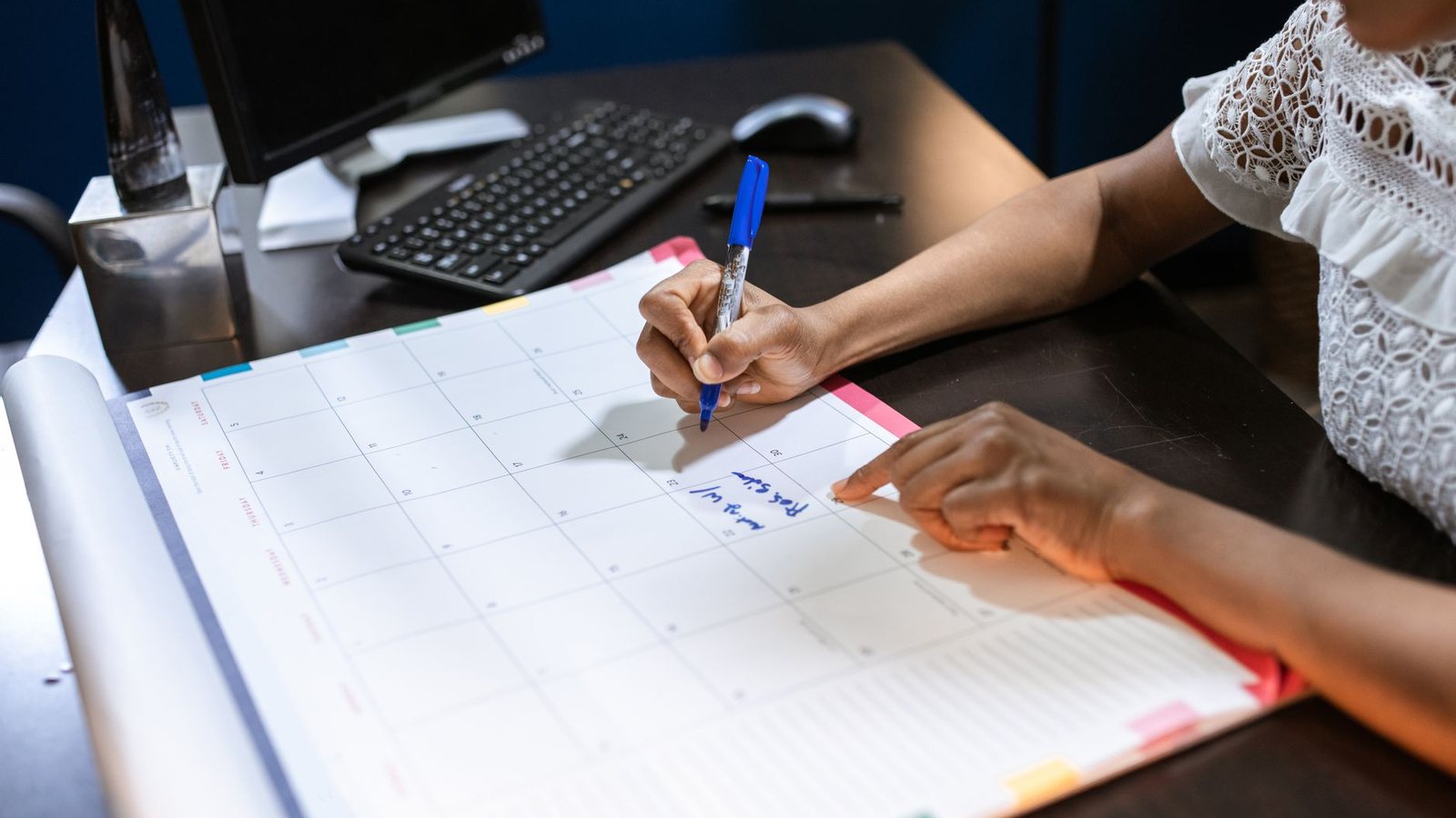 A hand writing a note into a desk calendar in an office, marking the dates a Belgian payroll runs on.