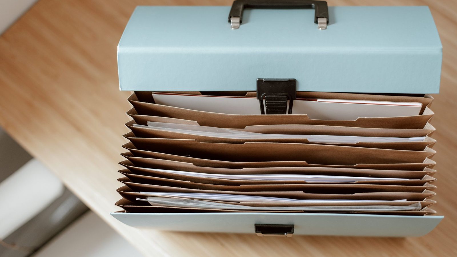 An expanding file box open on a wooden desk, its dividers filled with papers.