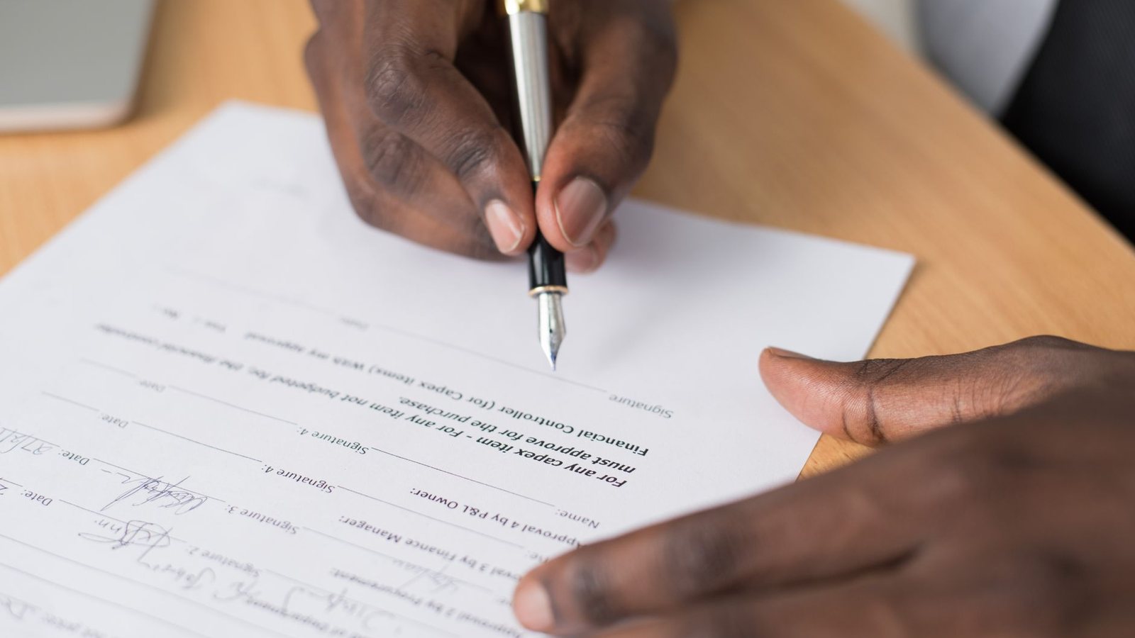 Close-up of a man's hands signing a formal document indoors, the kind of instrument that funds a representative's security.